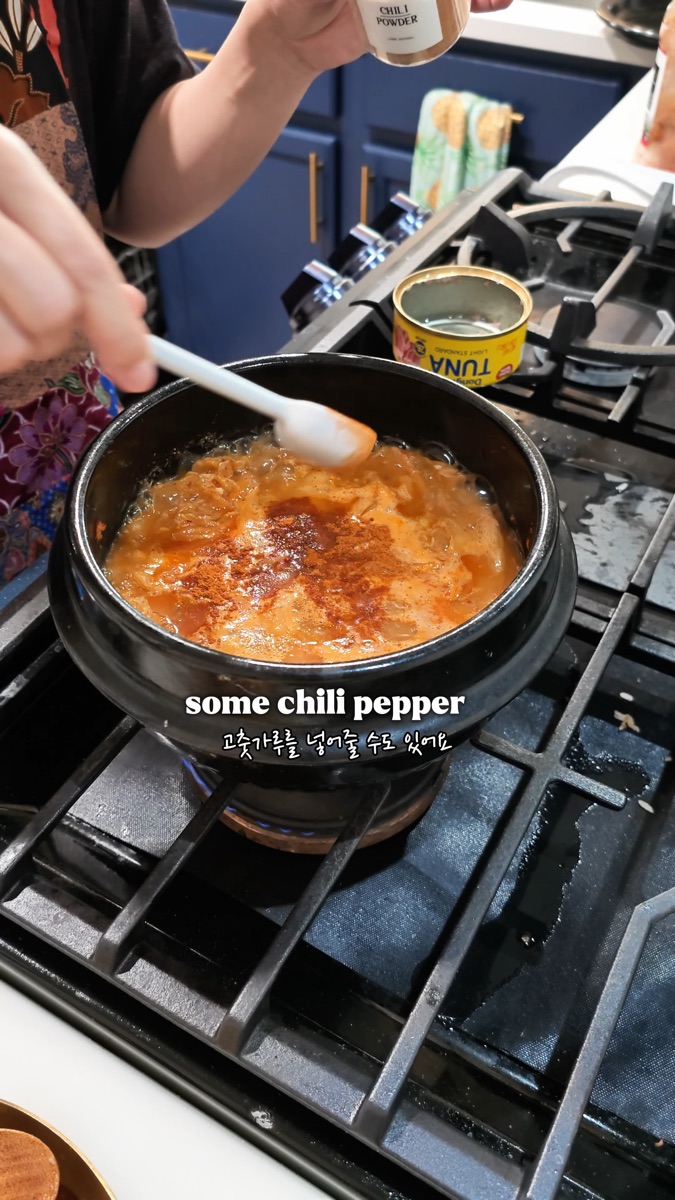 Tuna kimchi jjigae boiling on the stove with a pinch of gochugaru added for color