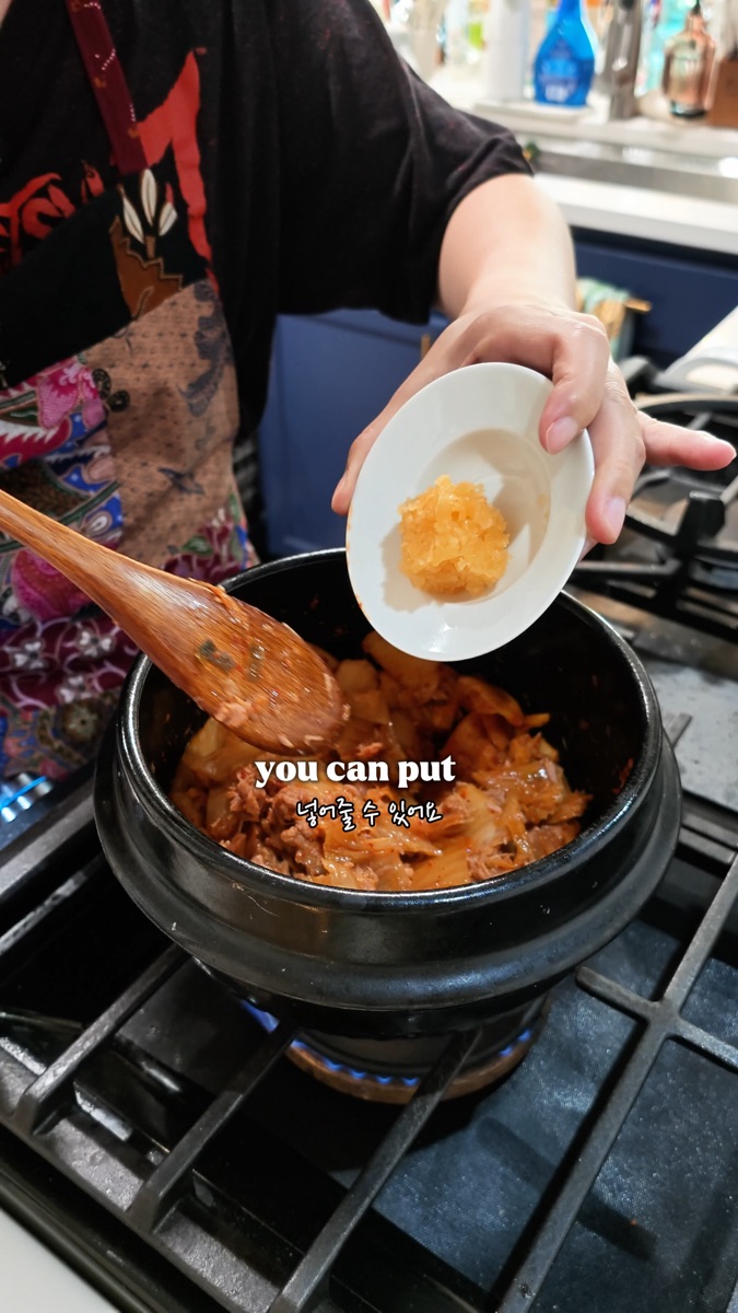 Adding minced garlic to the pot of stir-fried kimchi and tuna