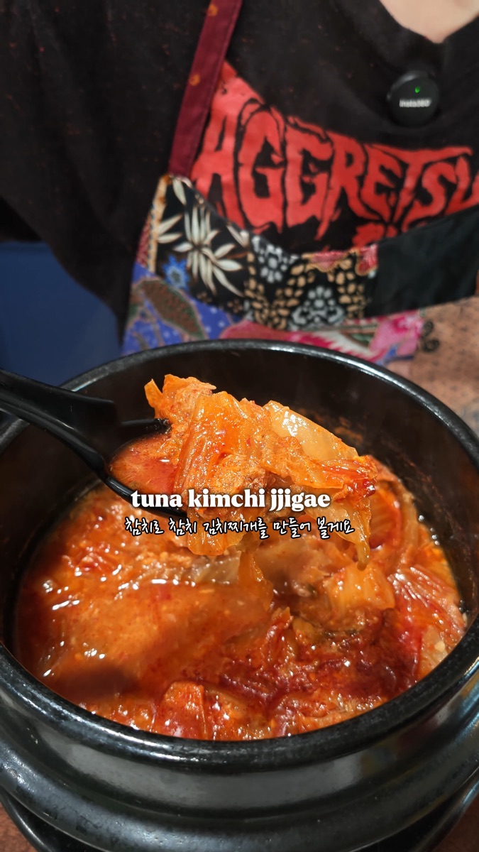 Tuna kimchi jjigae bubbling in a Korean earthenware pot, a spoonful of kimchi lifted from the stew
