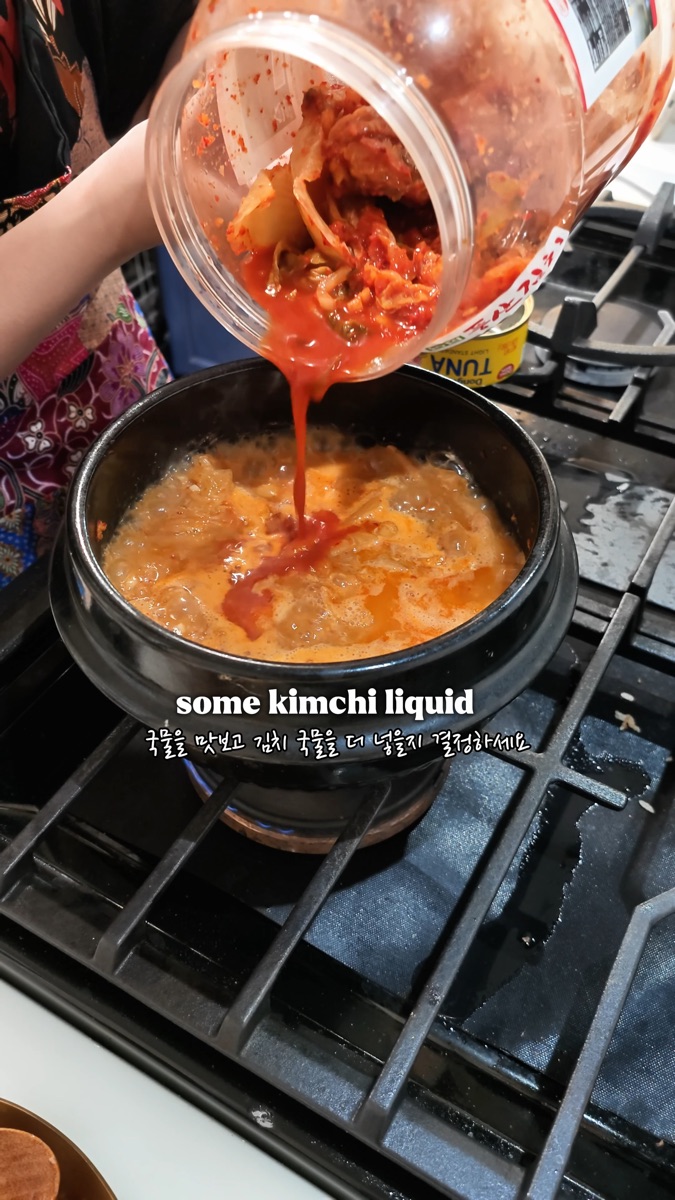 Pouring kimchi juice from the jar into the boiling pot of tuna kimchi stew