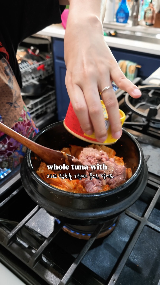 Adding a whole can of Korean tuna, oil included, into the pot with stir-fried kimchi
